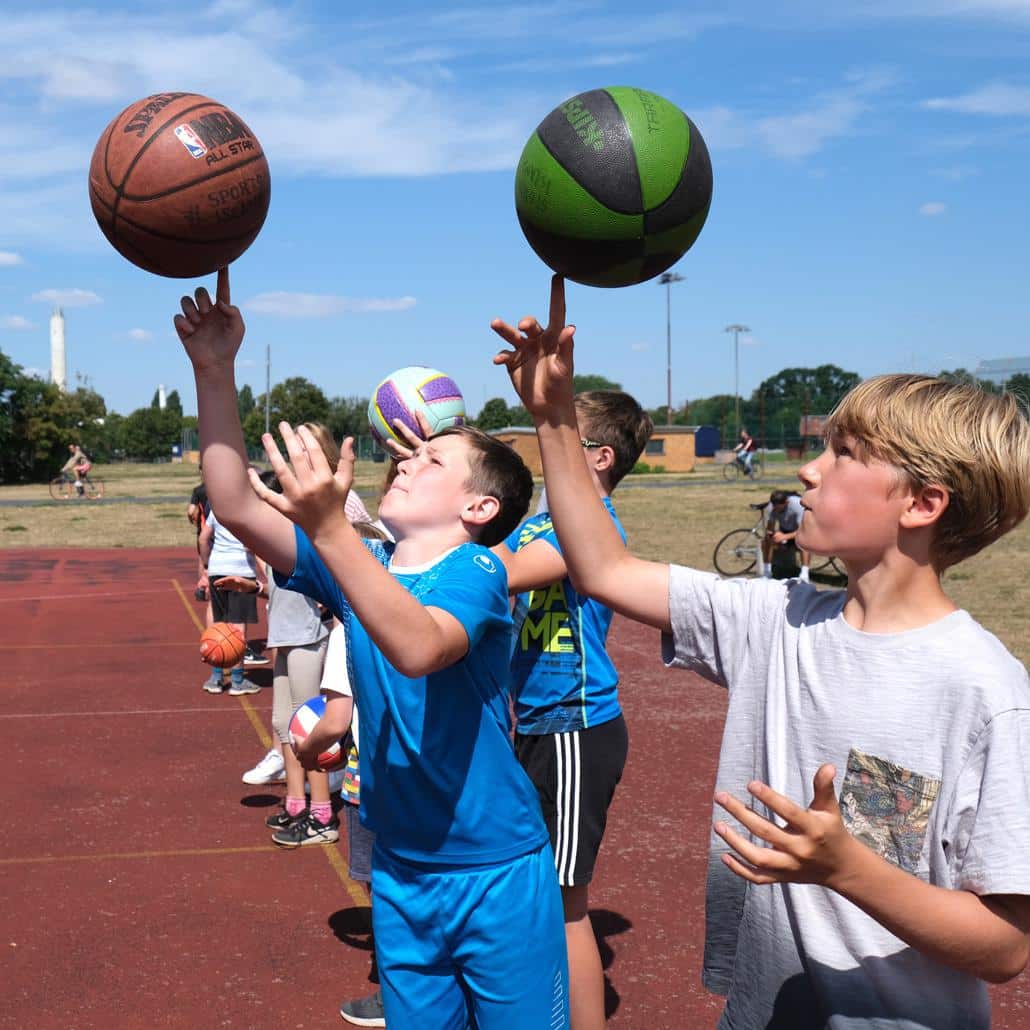 Kindere lassen den Basketball auf einen Finger laufen in den Feriencamps für Kinder