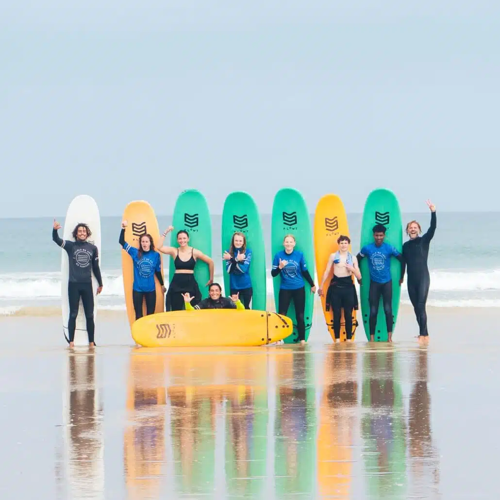 Teenager Gruppe winkt am Strand während der Herbstferien in den Herbstcamps mit Surfboards