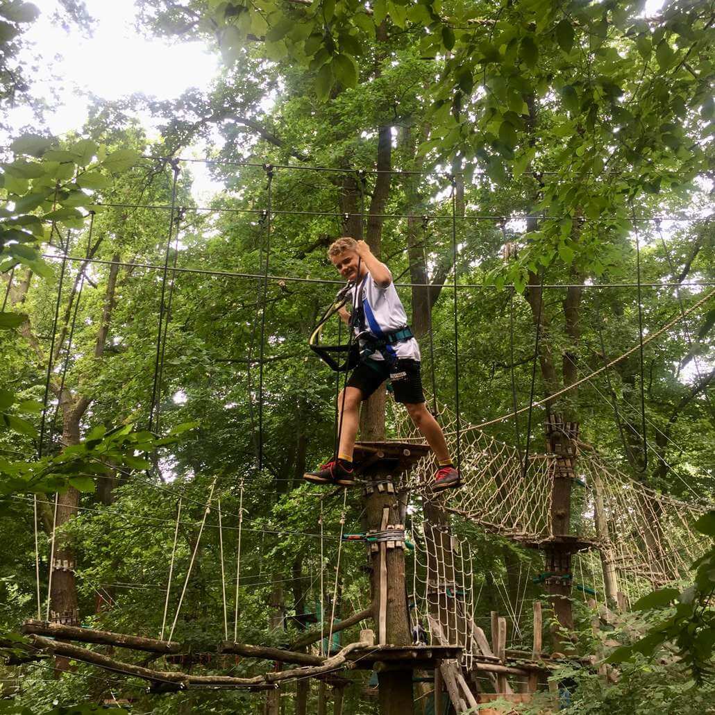 Kind im Sommercamp Potsdam #1 klettert im Kletterwald zwischen Bäumen