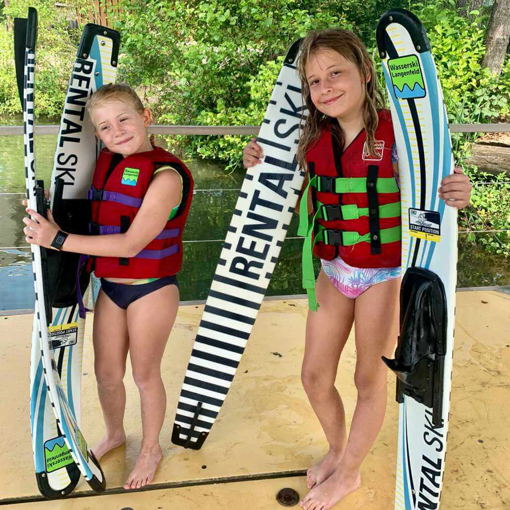 Sommercamp Köln #3 Blackfoot Beach: Zwei Mädchen mit Wasserskiern und Wakeboards haben Spaß