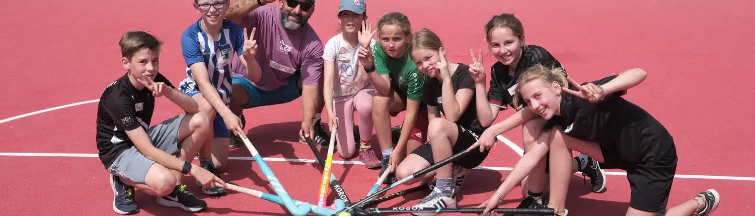Kinder und Coach kreuzen Hockeyschläger beim Team Sport & Racketsport Hockey im Sportcamp