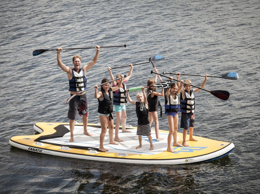 Coole Sportarten beim Wassersport: Kinder und Coach auf Stand Up Paddling Tour mit Paddel in der Luft